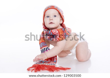 Smiling baby in knitted hat, scarf and diaper sitting on the floor. On a white background with reflection
