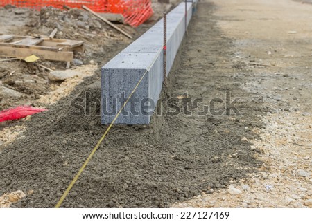 Large grey granite curb stone and string with stakes to level at road construction site. Selective focus.