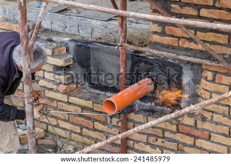 BELGRADE, SERBIA - DECEMBER 26: Insulation worker with propane blow torch melting bitumen felt around pipe on the basement wall. At construction site in December 2014.