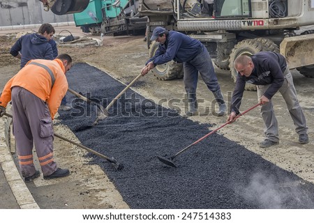 BELGRADE, SERBIA - JANUARY 21: Road construction crew used shovels to scatter more asphalt over the top of the new pavement.  At road construction site in January 2015. Selective focus.