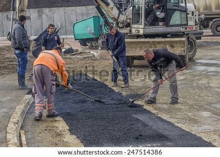 BELGRADE, SERBIA - JANUARY 21: Road construction crew used shovels to scatter more asphalt over the top of the new pavement. Selective focus. At road construction site in January 2015.