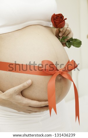 Pregnant woman holding red flowers tied with red ribbon to give as a gift to her husband.