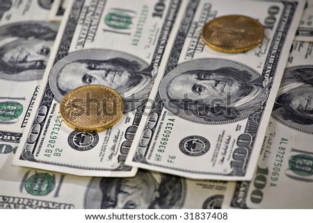 Two gold coins stacked on one hundred dollars bills.  St. Gaudens gold Double Eagle and Franklin one hundred dollar FRN (Federal Reserve Notes) are seen in the image.