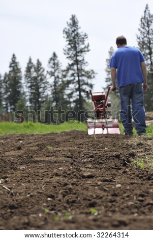 Man rototilling the ground, getting it ready for a garden.  Low vantage point.  Shallow DOF.