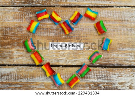 Happy birthday card with heart made of colorful candies on wooden surface