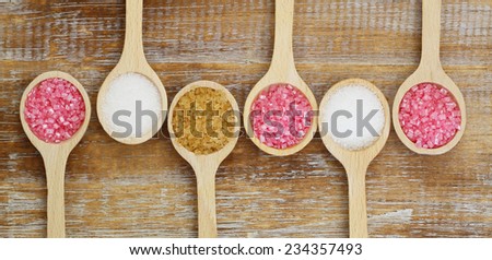 White, brown and pink sugar on wooden spoons on rustic wooden surface
