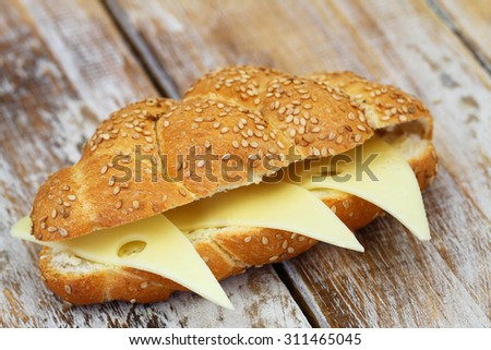 Crunchy sesame seeds bread roll with Swiss cheese on rustic wooden surface