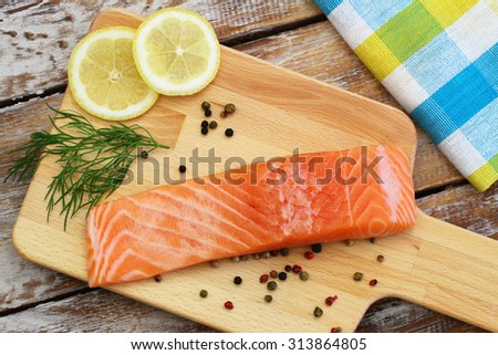 Raw salmon steak, lemon, fresh dill and black pepper on wooden board
