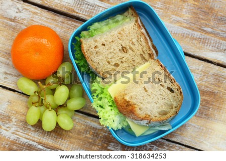 Healthy lunch box containing rustic bread sandwiches with cheese and lettuce, grapes and mandarine