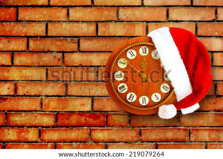 Santa Claus hat on New Year\'s night on the old clock showing twelve o\'clock on the brick background