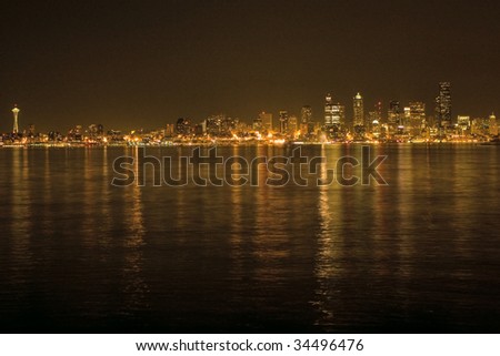 Seattle Skyline with Space Needle with Night Lights across the waters of the Puget Sound. The buildings and waters are lit up in the skyscrapers on this picturesque background.