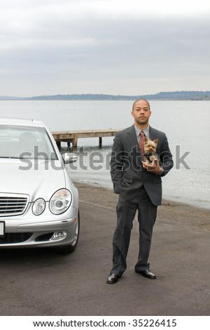 Ethnic Business Man and Yorkshire Terrier Dog are standing next to the lake. He is dressed in a suit and tie and is holding the dog.