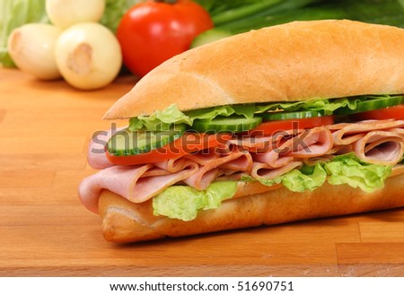 A large ham and tomato sandwich, on a wooden board