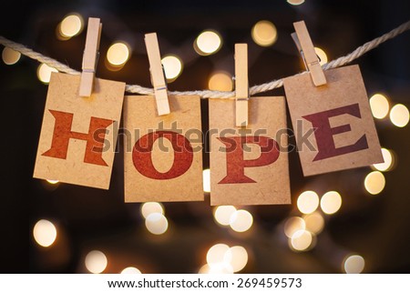 The word HOPE spelled out on clothespin clipped cards in front of glowing lights.