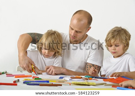 Father teaches his young son how to use a scissors. The father\'s upper arms are tattooed.