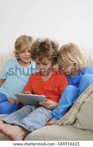 An 8-9 year old is playing a game on a touch screen tablet. His younger brothers are watching every move intently