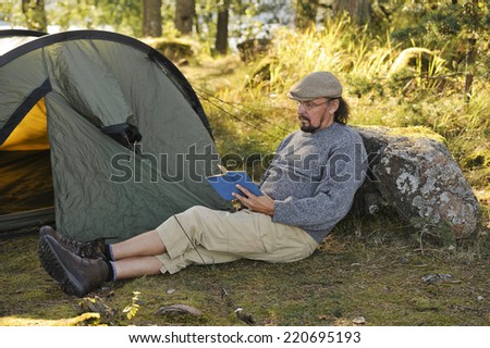 Senior man sits outside a tent and reads a book. There\'s digital filter flare