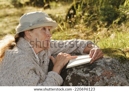 Senior woman sits outside her tent reading a book. There's some digital filter flare