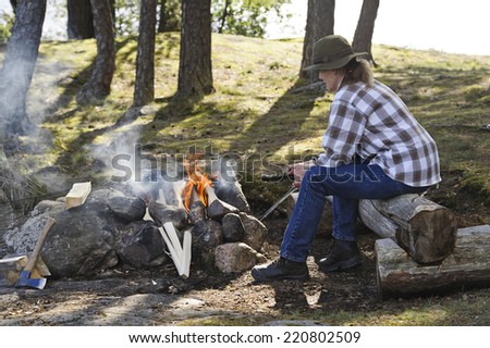 Senior couple light a camp fire. They are in a forest beside a lake