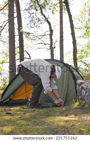 Senior man pitches a tent in forest beside a lake