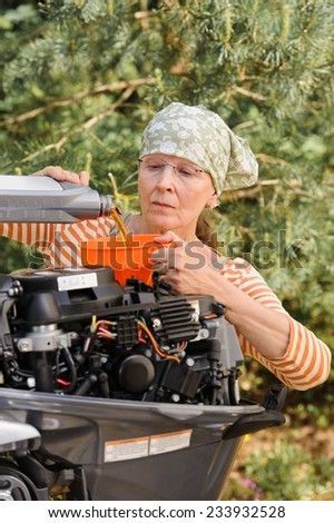 Senior woman pours oil into an outboard engine through a funnel. Breaking down the  stereotypes of women - gender and age