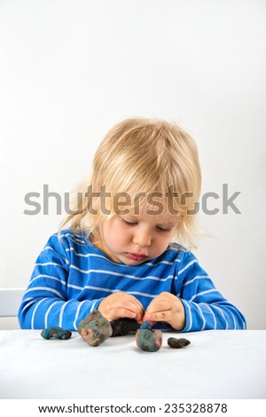 Young boy sits at a table and plays with plasticine. He\'s learning to build objects.