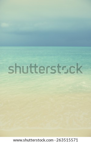 Blurred sea and sand with turquoise seas and dark clouds on the horizon.Designed to work with text overlays including the text colour white. Artistic intent with filters and desaturation.