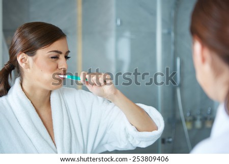 Young pretty woman brushing teeth in front of the mirror