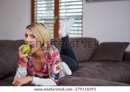 Close up portrait of young woman with with a apple in her hand on a sofa