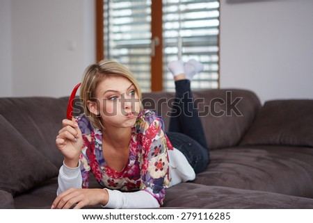 Close up portrait of young woman with with a chilli in her hand on a sofa