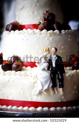 a little bride and groom sit on this strawberry covered wedding cake ready to kiss
