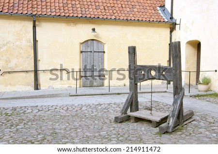 An old wooden lockup, pillory on a yard. Walls and setts, paves around.