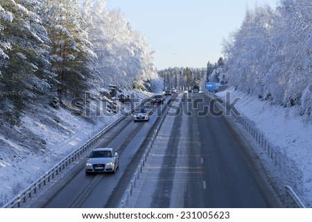 UMEA, SWEDEN ON NOVEMBER 05. Cars, vehicles, drives on a winter road on November 05, 2014 in Umea, Sweden. Frosty trees and a blue sign in the background. European Route 4.