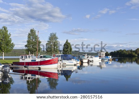GREAT-LAKE, SWEDEN ON JULY 02. View in a sunny evening at a small harbor on July 02, 2012 by the Great-Lake, Sweden. Calm water and the boats are moored by the bridge. Gazebo on the tip.