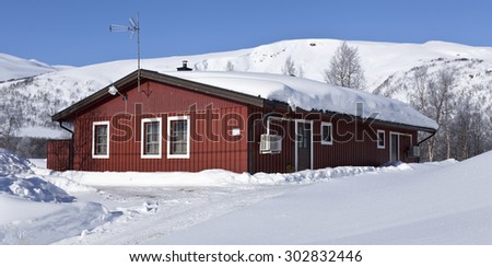 LAPLAND, SWEDEN ON MARCH 15. A red house on the mountainside a frosty morning on March 15, 2015 in Lapland, Sweden. Wintry white road, snowmobile tracks and rime in the trees.
