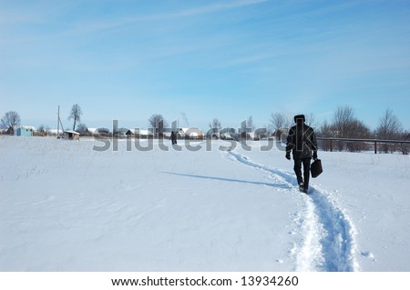 Man with a briefcase, following the winter path to a small russian village, sunny winter day