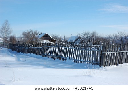View of small snowy russian village with old wooden fence at winter sunny day