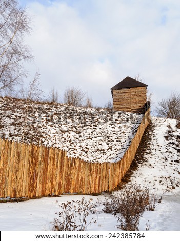 Rough wooden fence and a barn on the snow-covered hill, winter time
