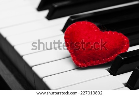 Red felt heart lays on white and black keys of the piano keyboard