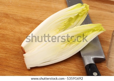 freshly cut chicory halves and a knife on a wooden cutting board