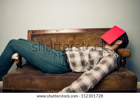 Man sleeping on old sofa with book covering his face