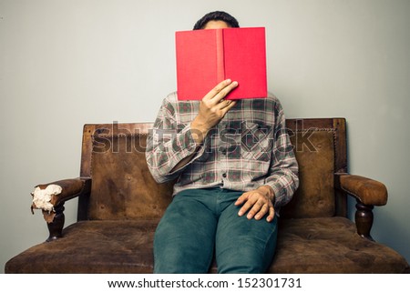 Man hiding behind book on old sofa