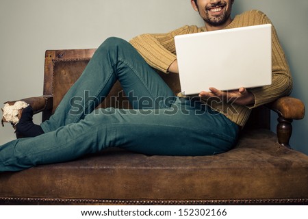 Smiling young man with laptop on old sofa