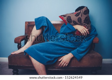 Man in dressing gown sleeping with face behind cushion