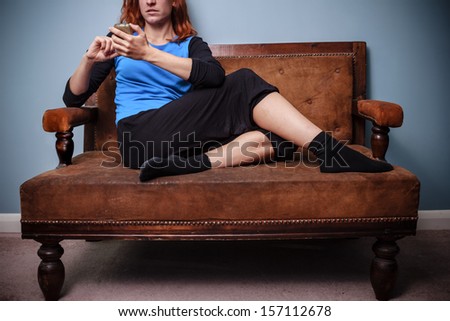 Young woman sitting on old sofa texting on her phone