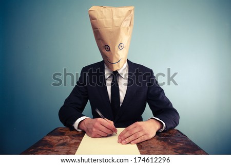 Businessman with bag over head writing at desk