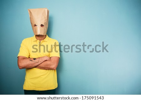Young man with a bag over his head standing with his arms crossed and looking grumpy
