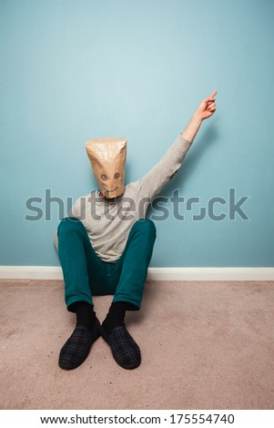 Man with a bag over his head is sitting on the floor and pointing