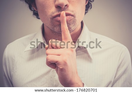 Young man with finger on lips is gesturing hush