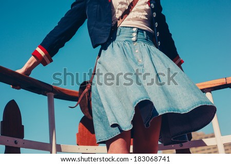 A young woman\'s skirt is blowing in the wind as she is standing on the deck of a boat cruising down the river